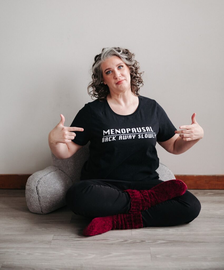 Coach Kristy sitting on the floor pointing towards her t-shirt that warns "Menopausal, back away slowly"